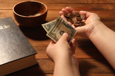 Photo of Donate and give concept. Woman holding coins and dollar banknote at wooden table, closeup