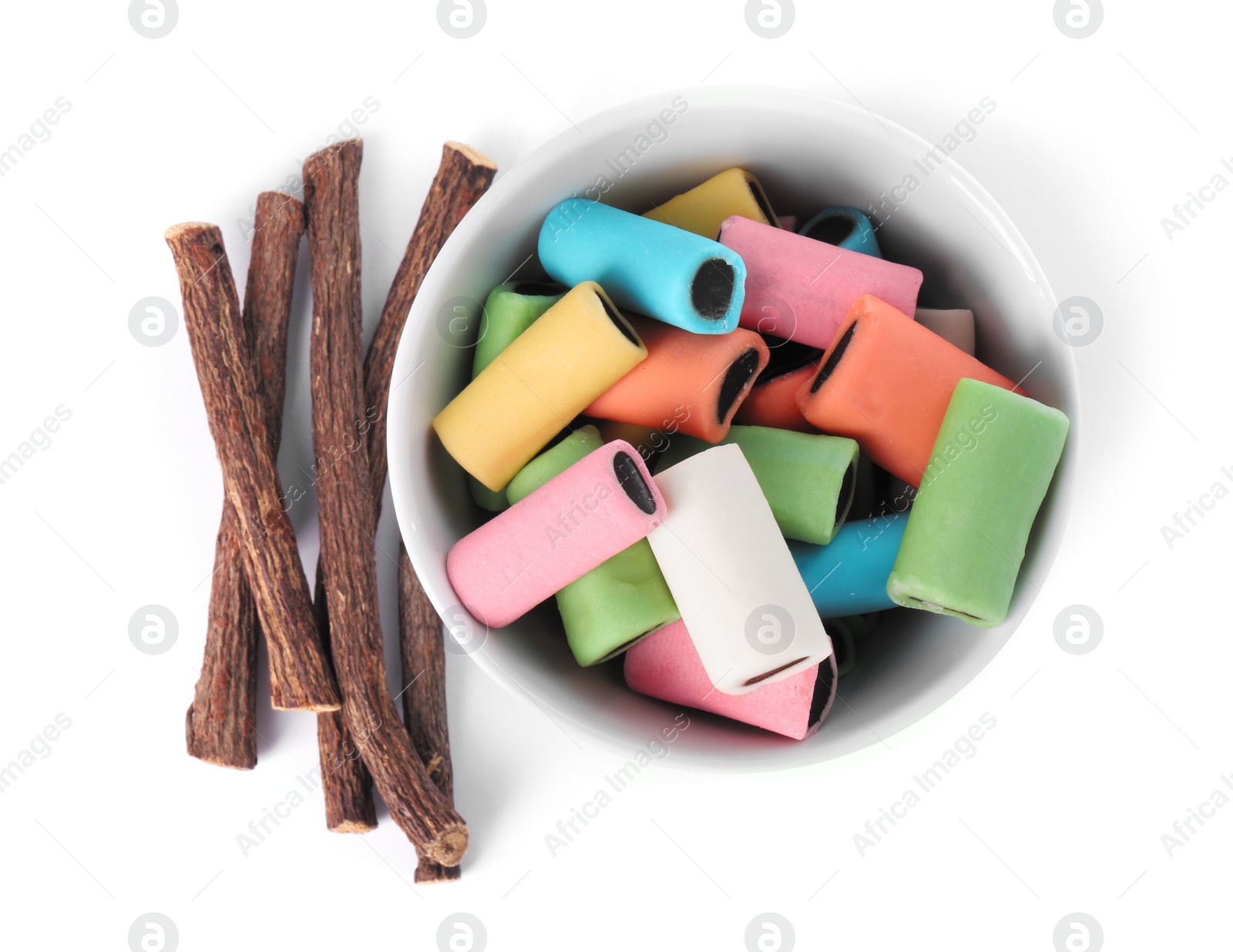 Photo of Bowl with many tasty candies and dried sticks of liquorice root isolated on white, top view