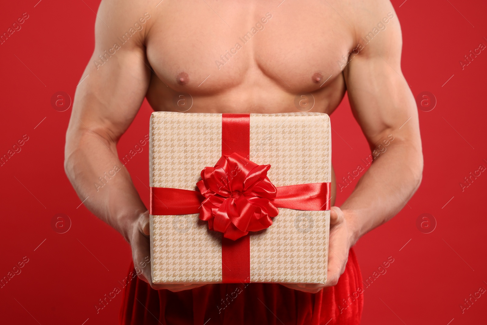 Photo of Young man with muscular body holding Christmas gift box on red background, closeup