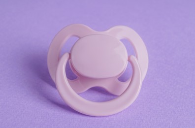 One new baby pacifier on purple background, closeup