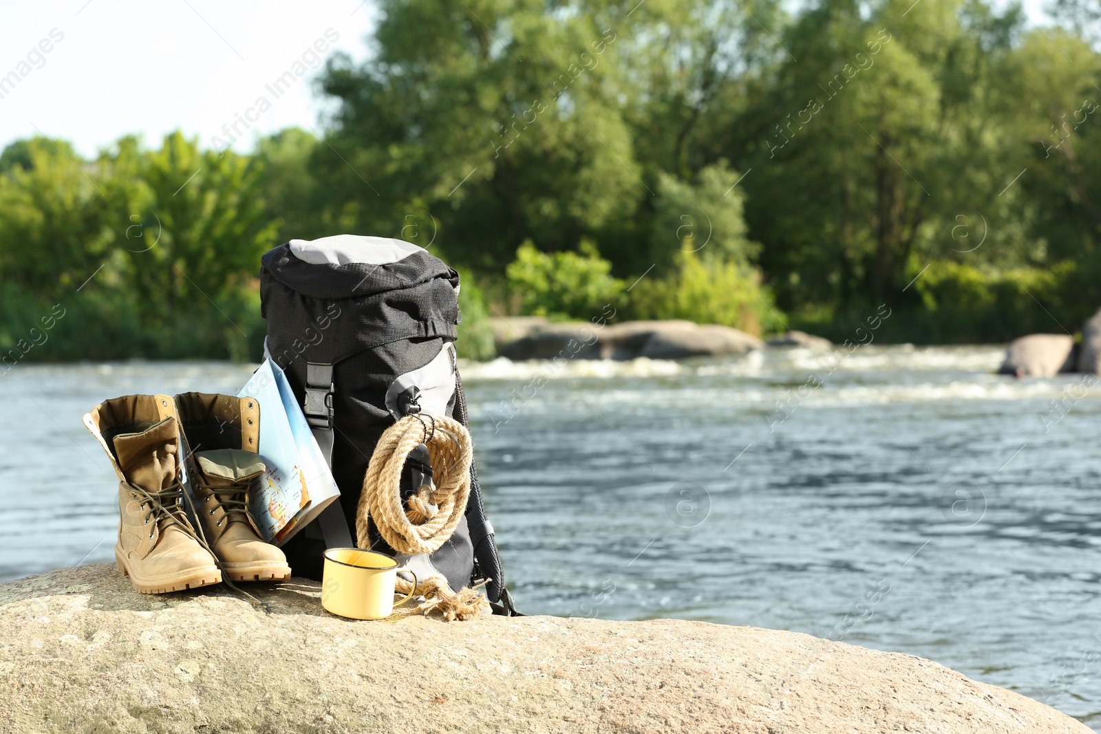 Photo of Backpack and camping equipment on rock near river. Space for text