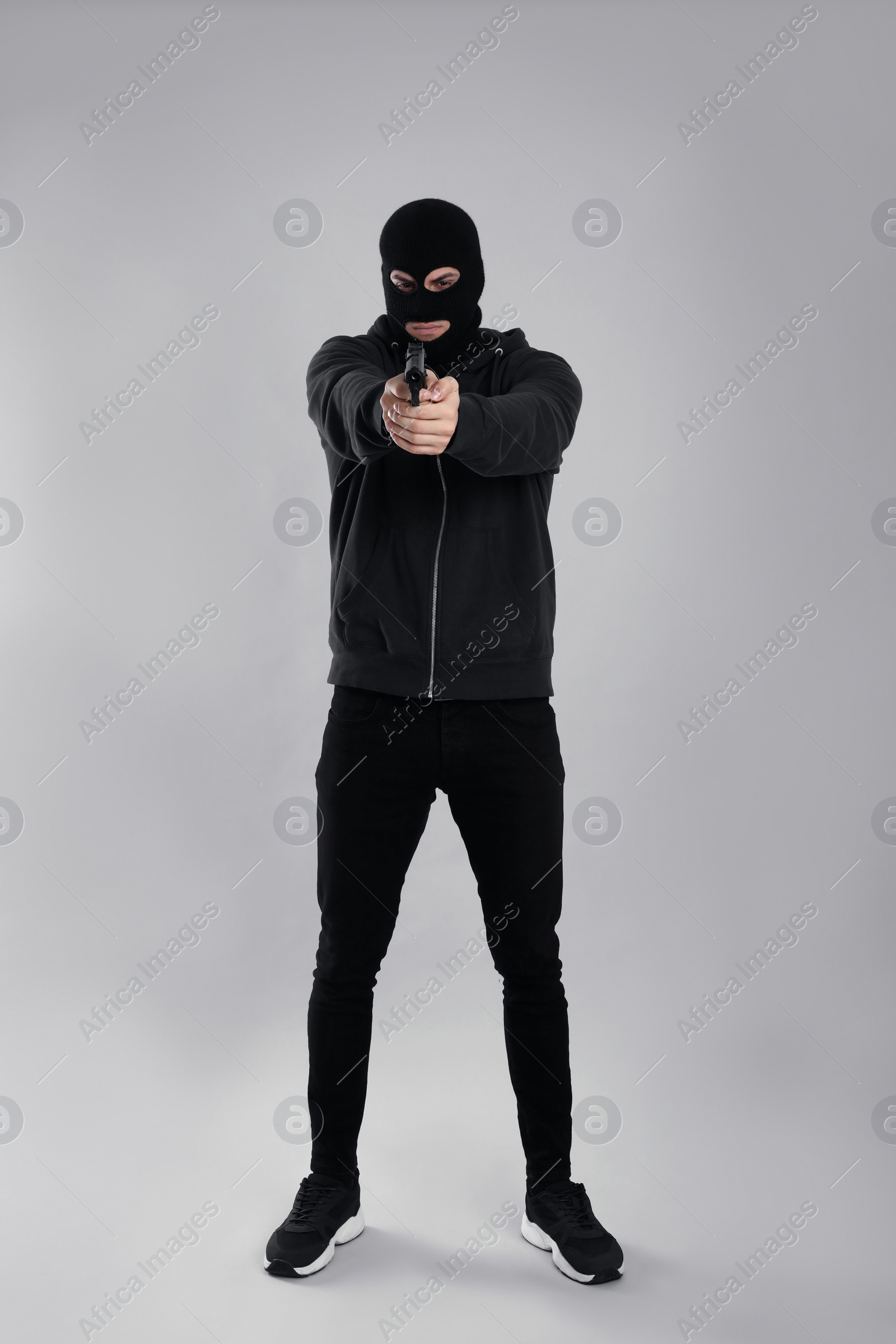 Photo of Man wearing black balaclava with gun on light grey background