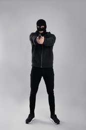 Man wearing black balaclava with gun on light grey background