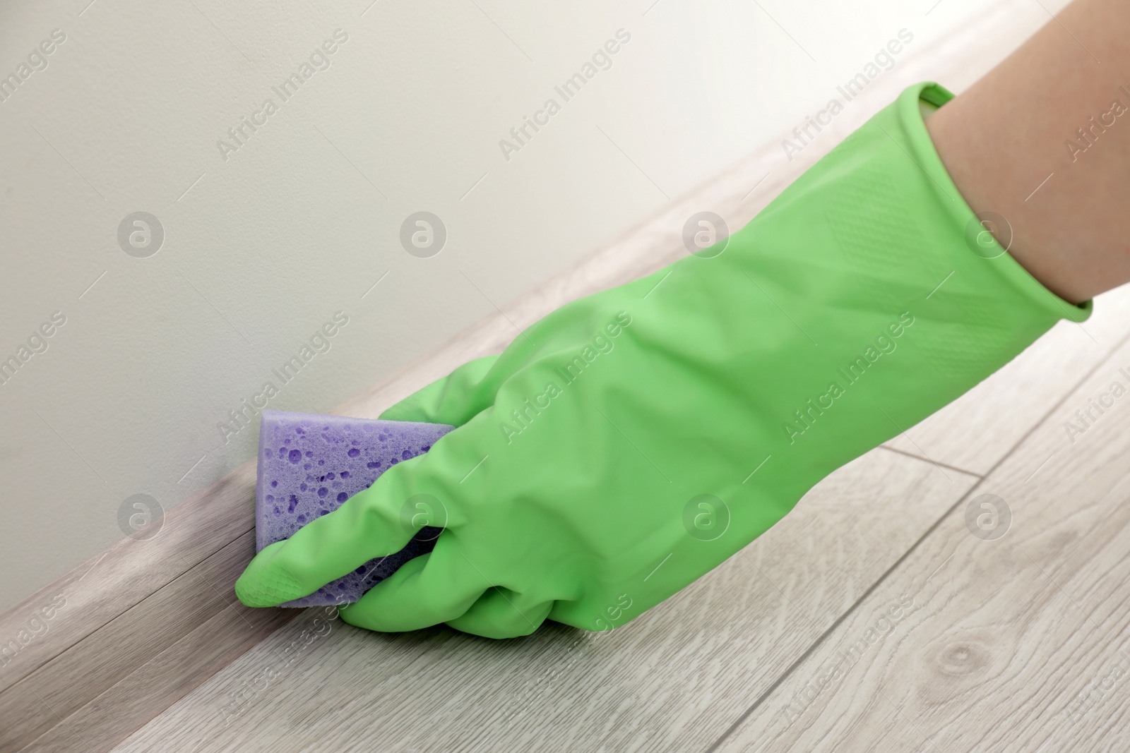 Photo of Woman in protective glove cleaning plinth with sponge indoors, closeup