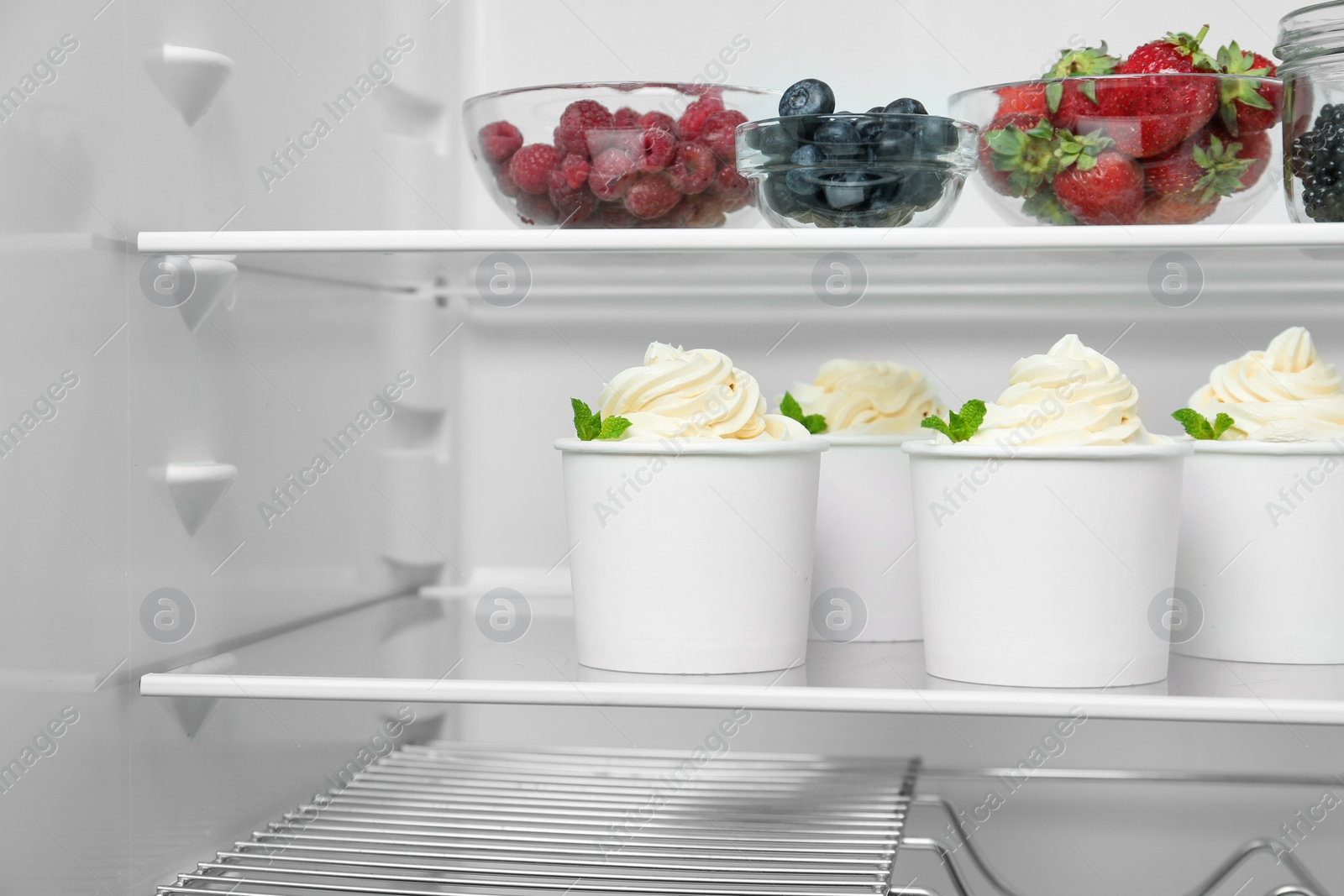 Photo of Cups with tasty frozen yogurt on fridge shelf