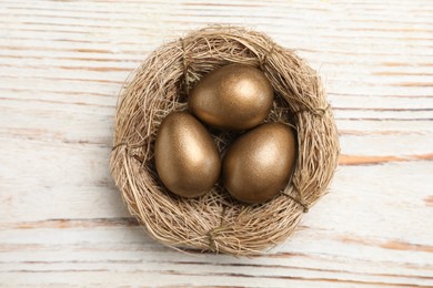 Photo of Golden eggs in nest on white wooden table, top view