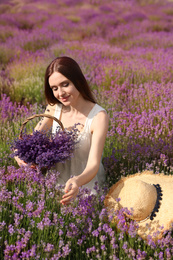 Photo of Young woman with straw hat and wicker basket full of lavender flowers in field