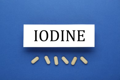 Photo of Card with iodine element and pills on blue background, flat lay