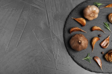 Photo of Slate plate with aged black garlic and rosemary on gray background, top view. Space for text
