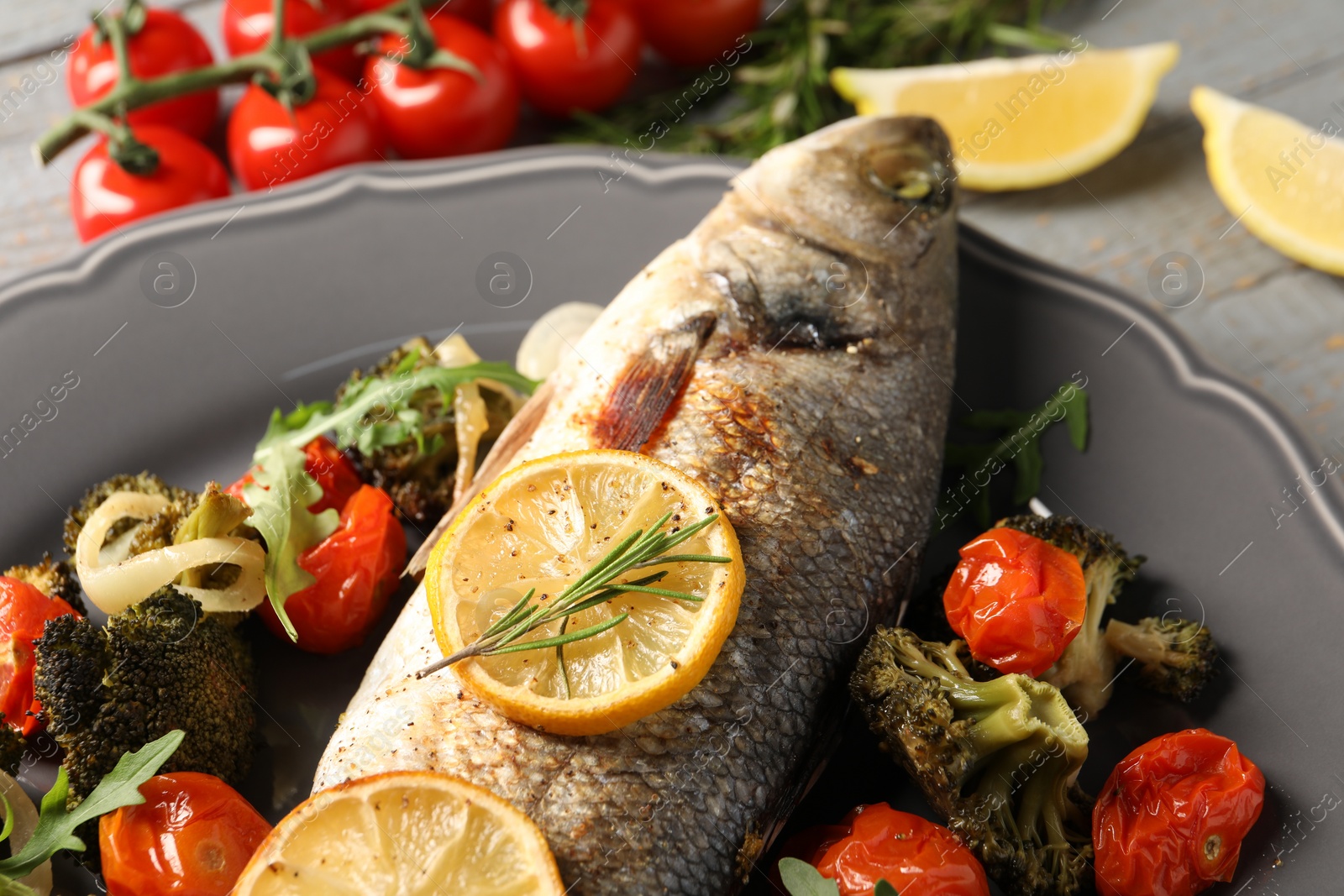 Photo of Baked fish with vegetables, rosemary and lemon on grey wooden table, closeup