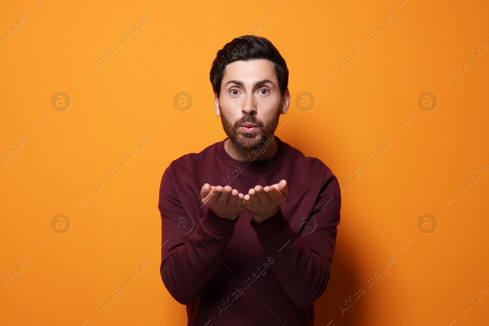 Photo of Handsome man blowing kiss on orange background