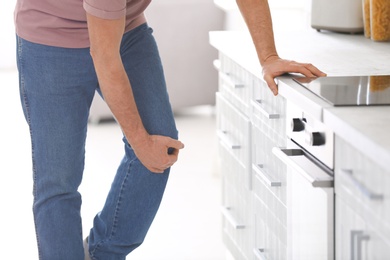 Photo of Senior man suffering from knee pain in kitchen, closeup. Space for text