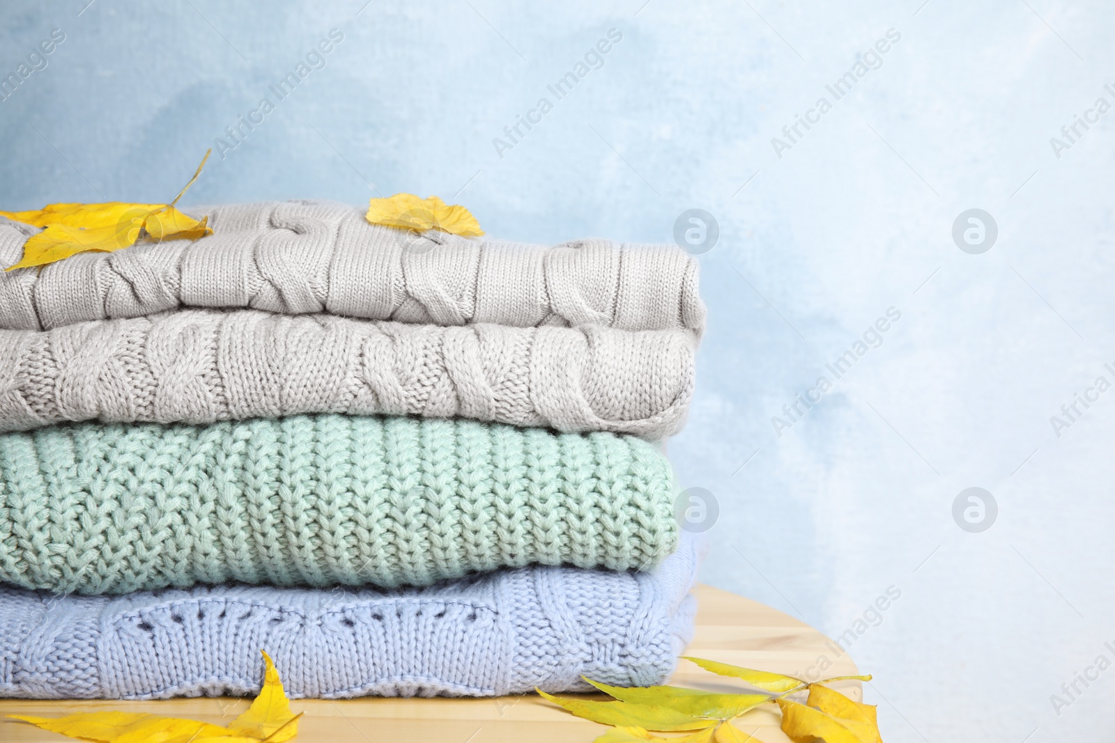 Photo of Stack of warm clothes and autumn leaves on wooden table against light blue background, space for text