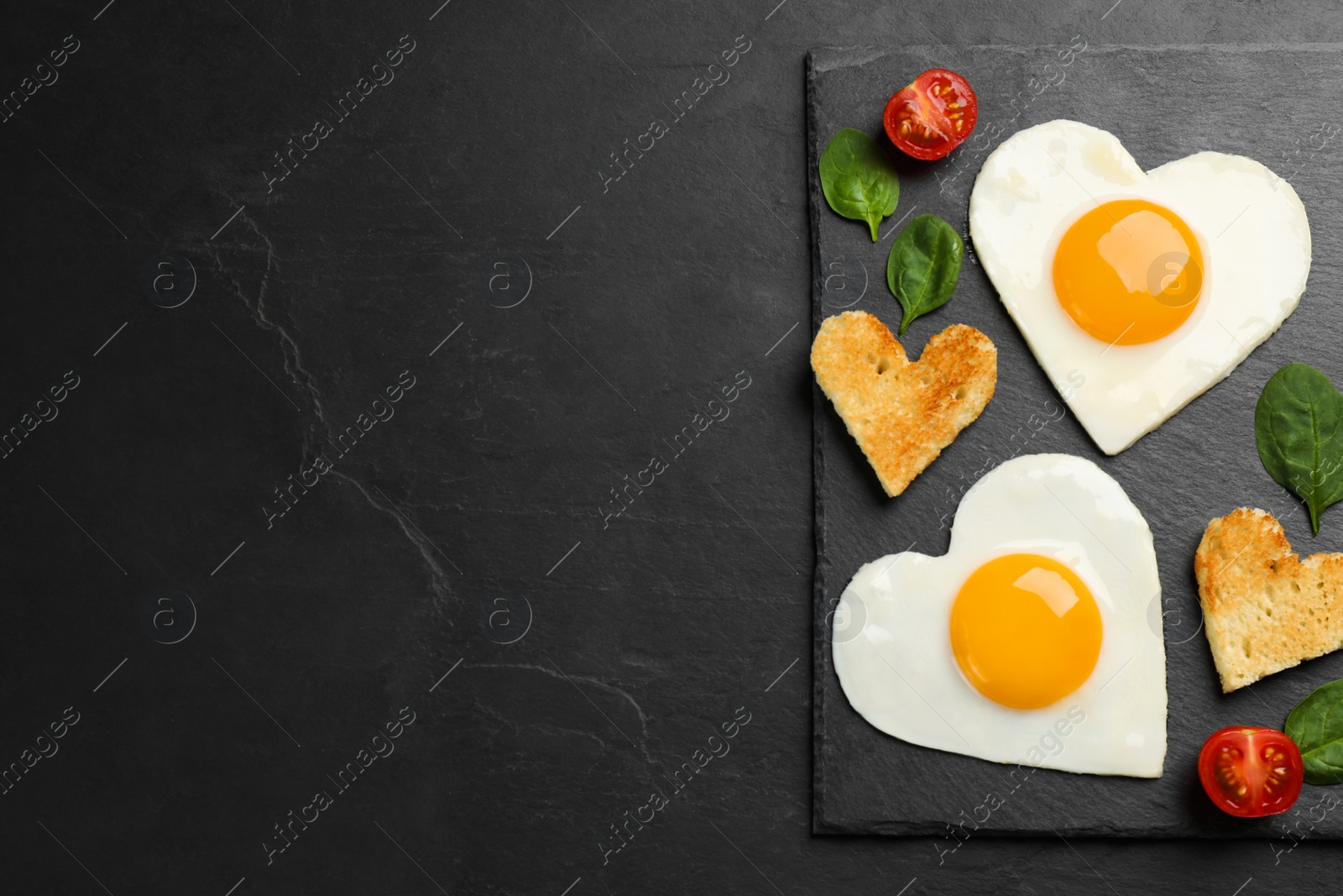 Photo of Heart shaped fried eggs and toasts on black table, top view. Space for text