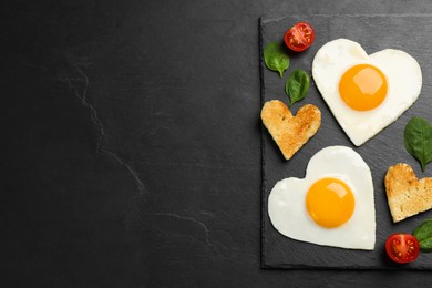 Photo of Heart shaped fried eggs and toasts on black table, top view. Space for text