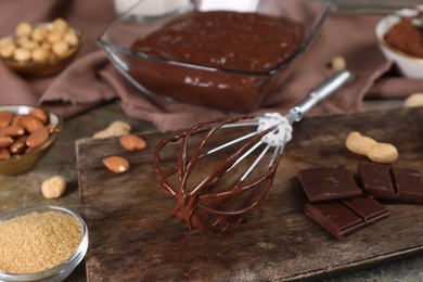 Whisk with chocolate cream and ingredients on grey table, closeup