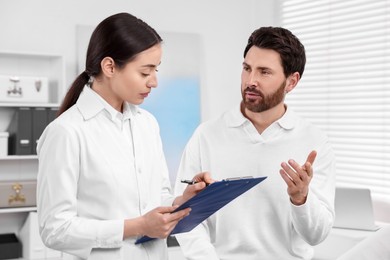 Doctor with clipboard consulting patient during appointment in clinic