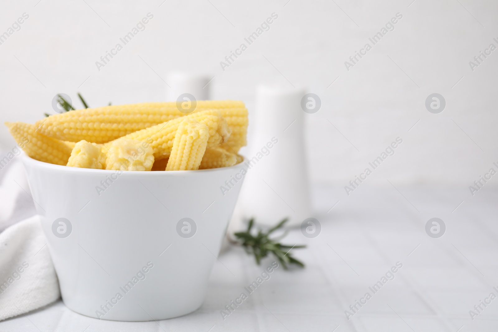 Photo of Tasty fresh yellow baby corns in bowl on white tiled table, space for text