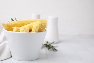 Tasty fresh yellow baby corns in bowl on white tiled table, space for text