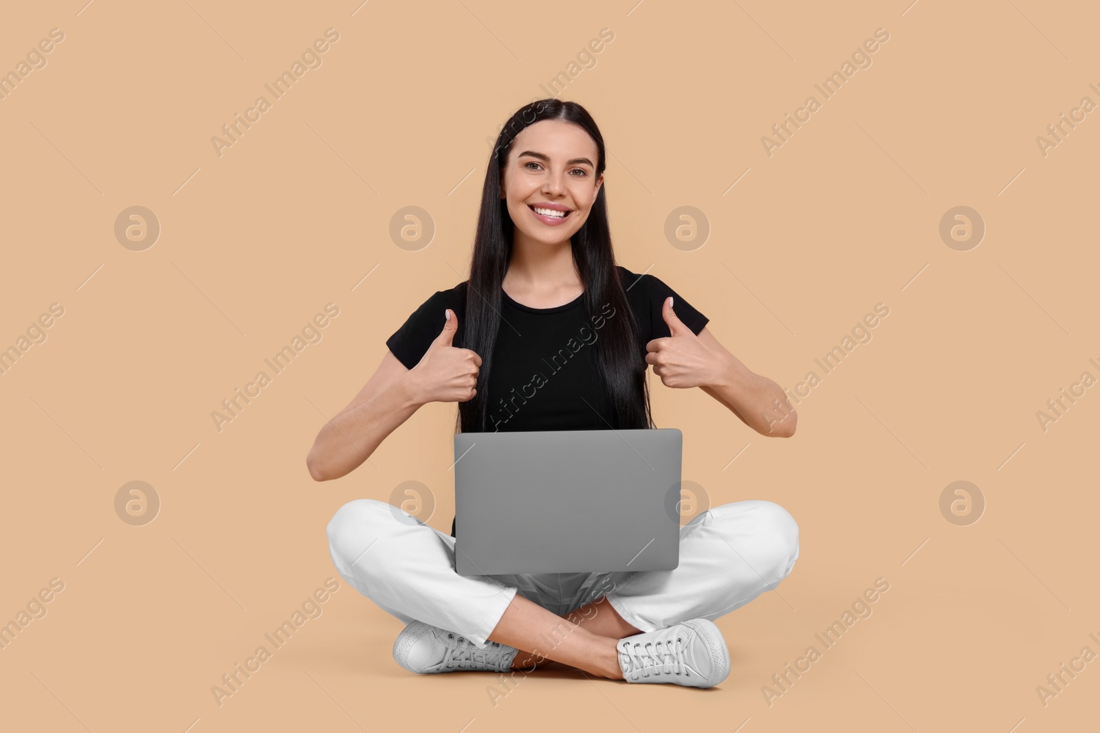 Photo of Happy woman with laptop showing thumbs up on beige background