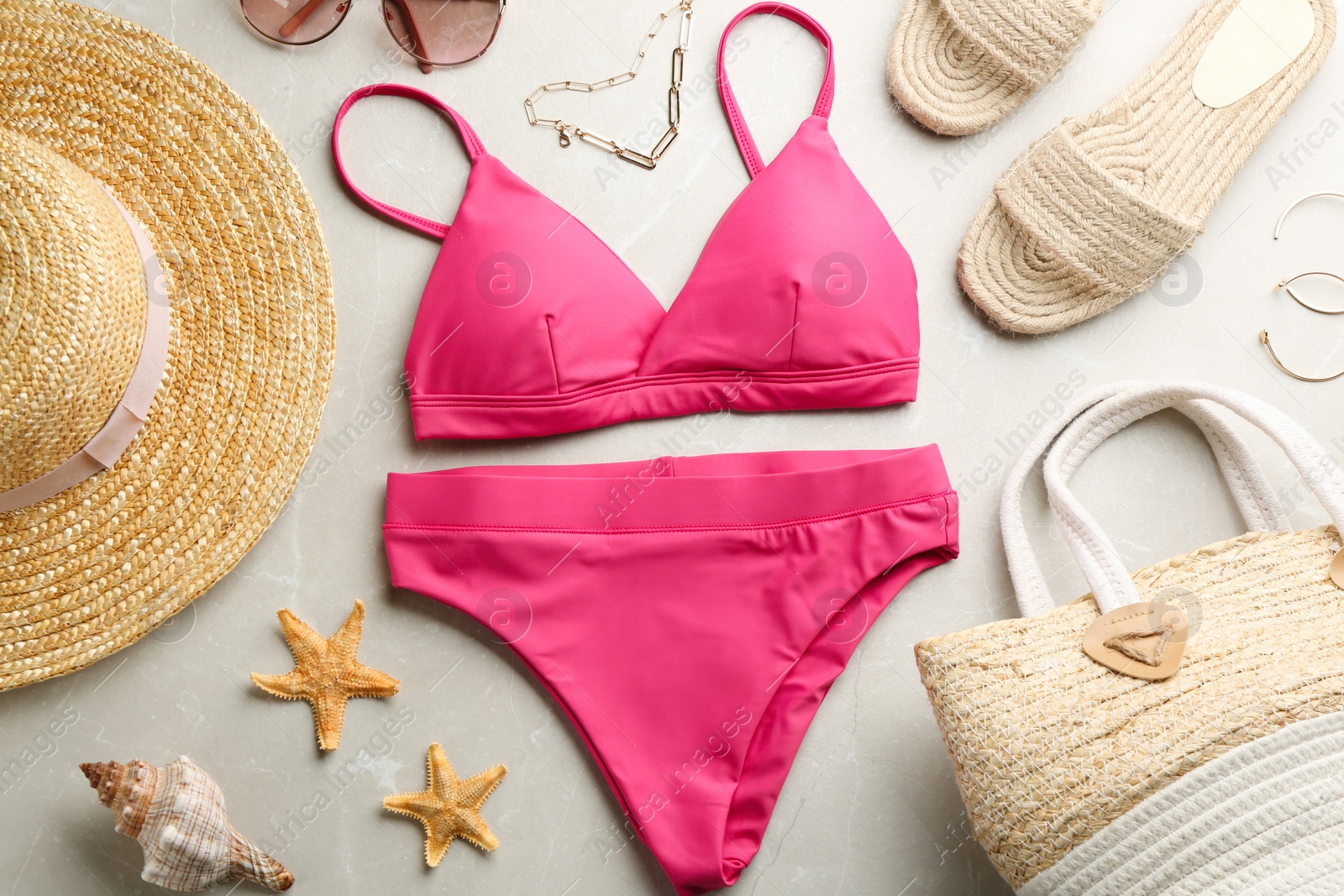 Photo of Beautiful pink bikini and beach accessories on light marble background, flat lay