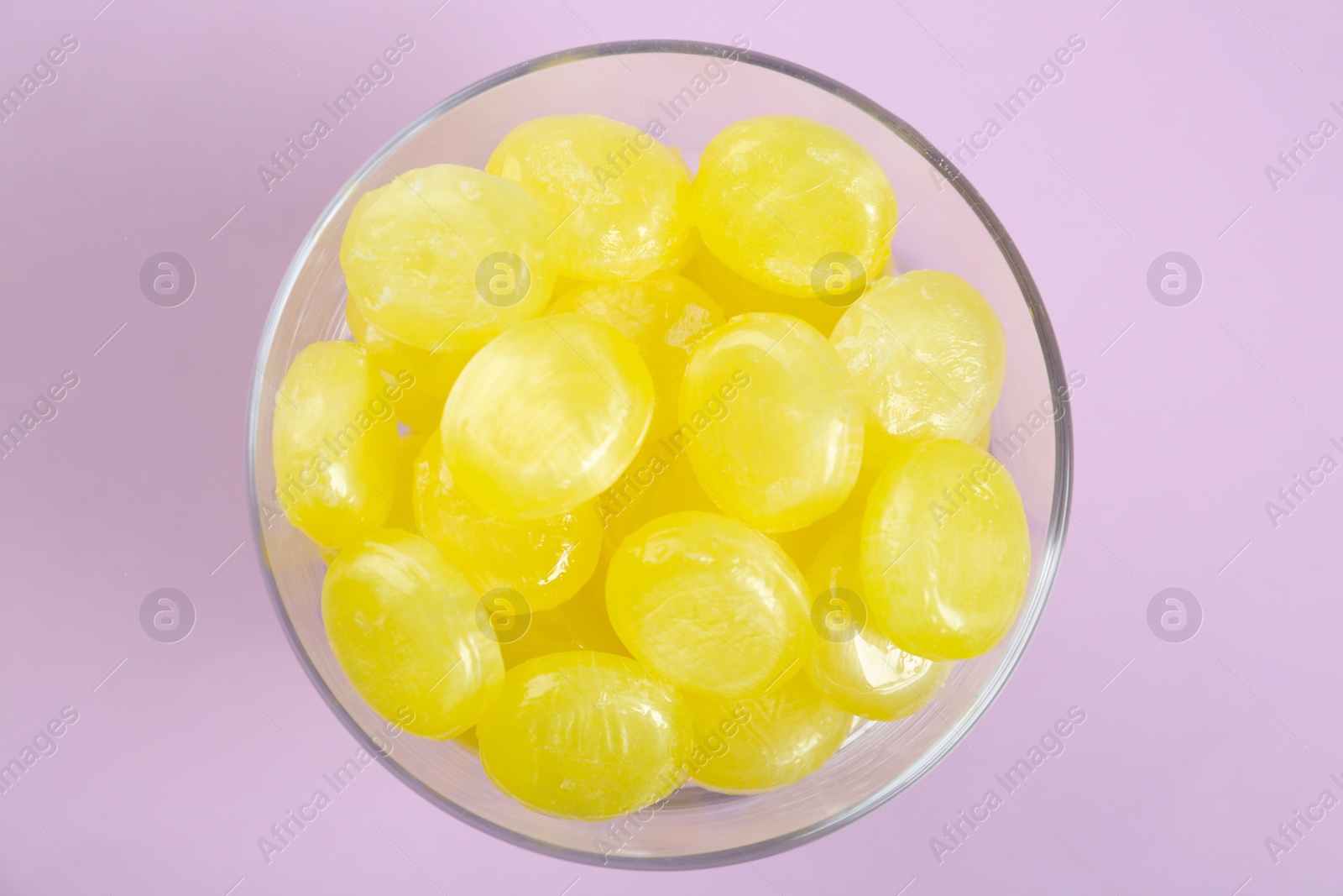 Photo of Tasty lemon drops in bowl on violet background, top view