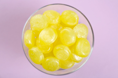 Tasty lemon drops in bowl on violet background, top view