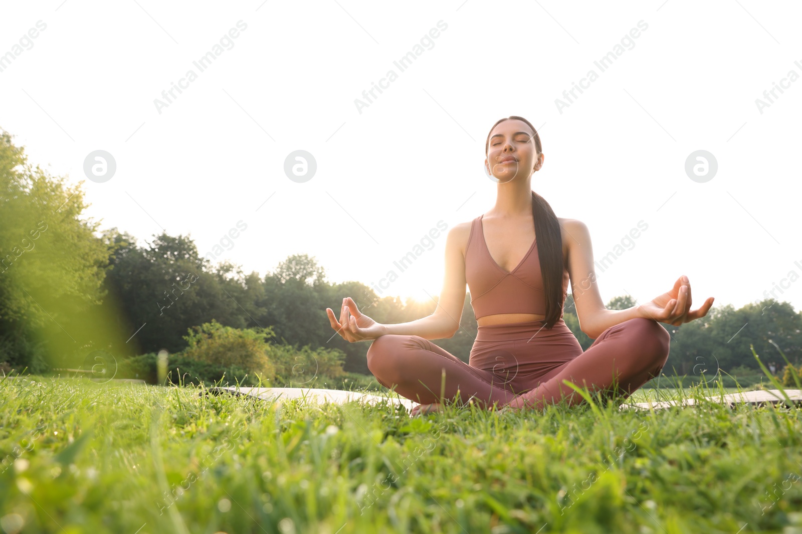 Photo of Beautiful young woman practicing Padmasana on yoga mat outdoors, low angle view. Lotus pose