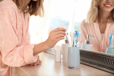 Photo of Young woman taking toothbrush from holder in bathroom. Personal hygiene