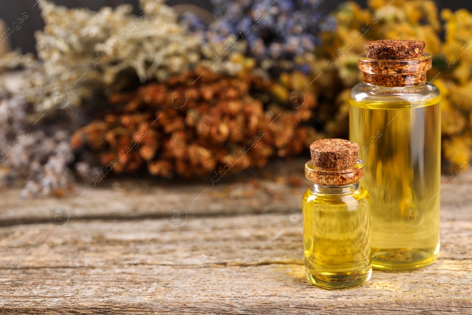 Photo of Bottles of essential oils and many different dry herbs on wooden table, closeup. Space for text