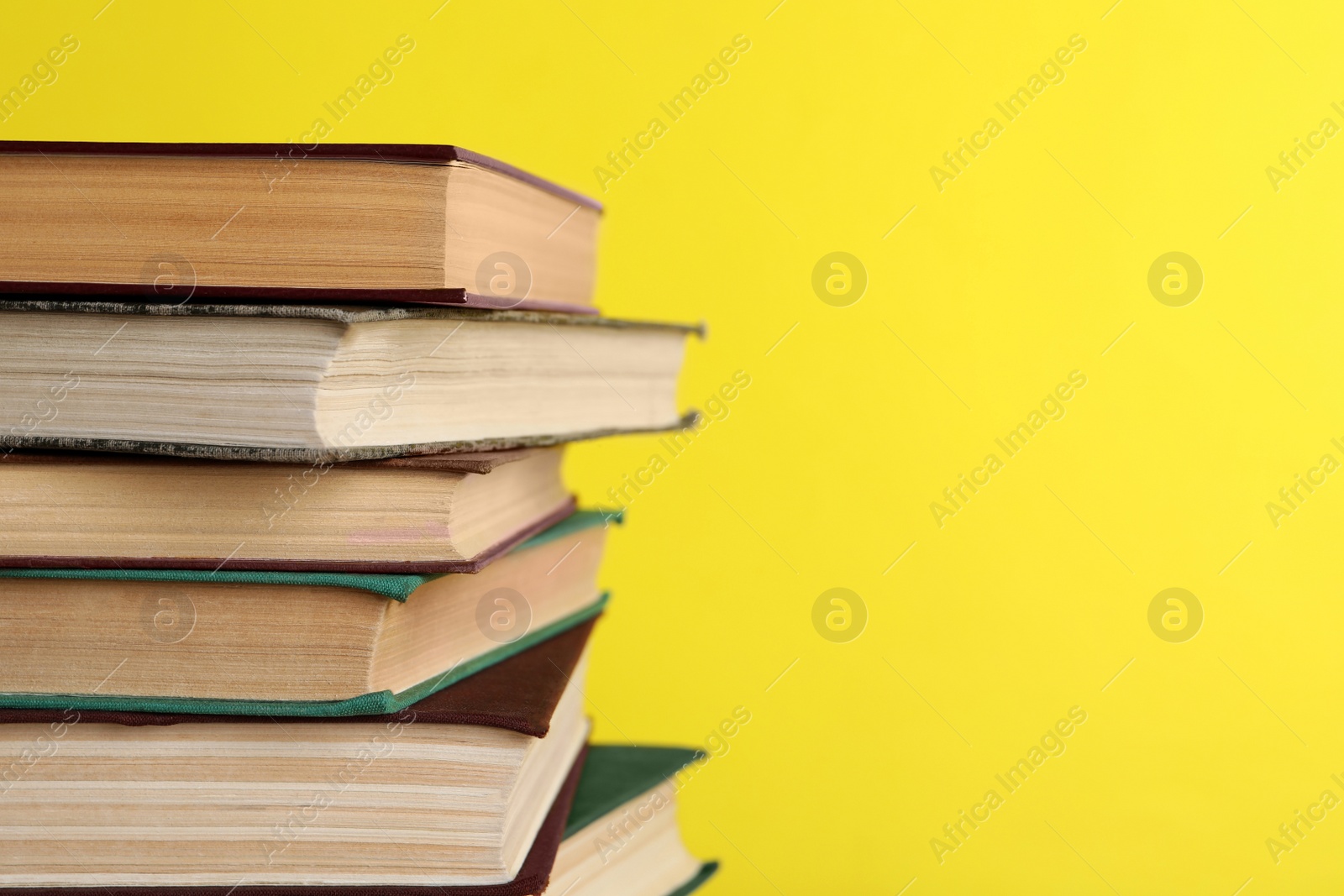 Photo of Stack of old hardcover books on yellow background, closeup. Space for text