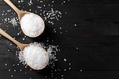 Photo of Organic salt in spoons on black wooden table, top view. Space for text