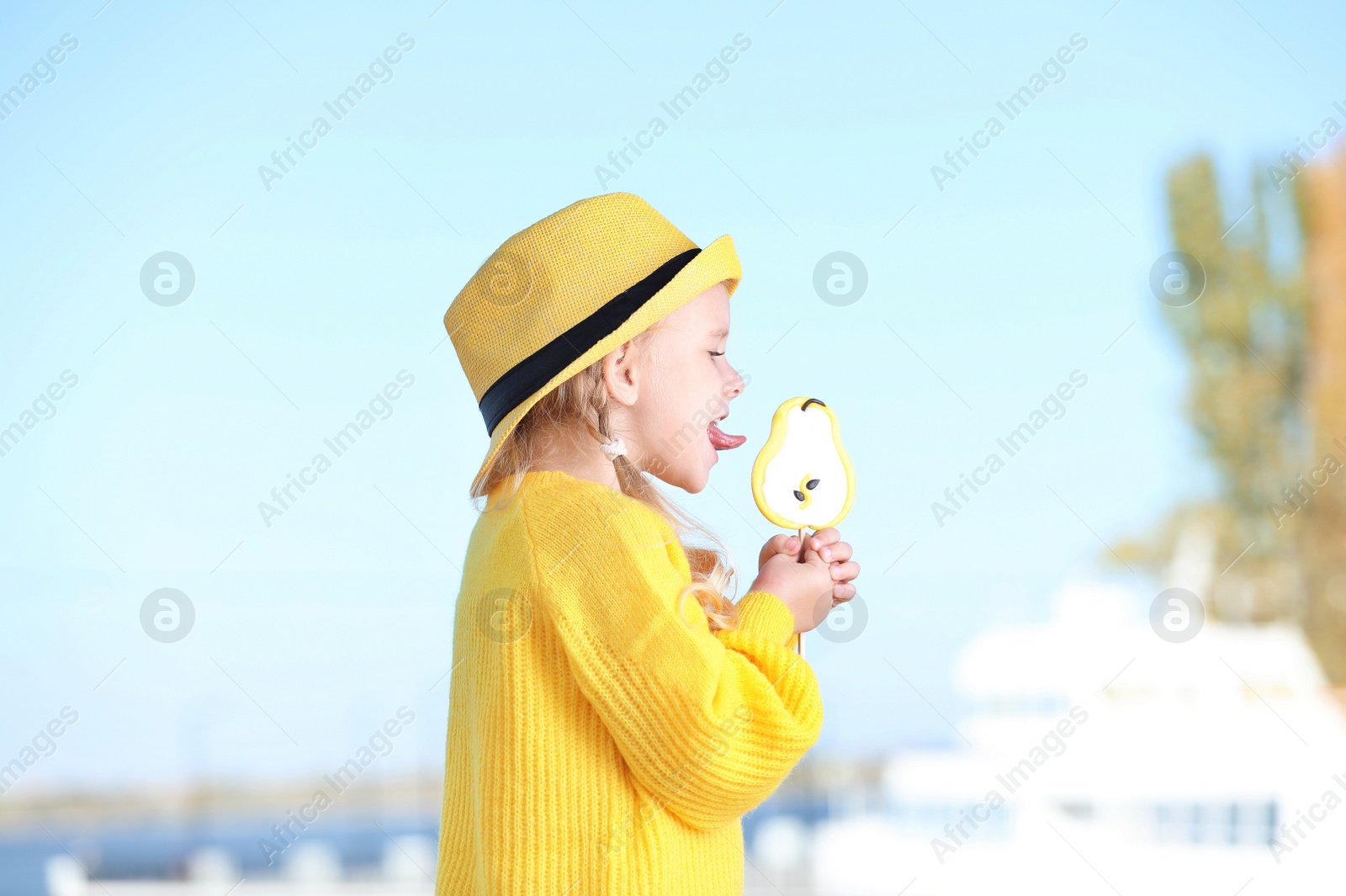 Photo of Cute little girl with tasty candy outdoors