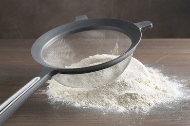 Photo of Sieve and pile of flour on wooden table, closeup