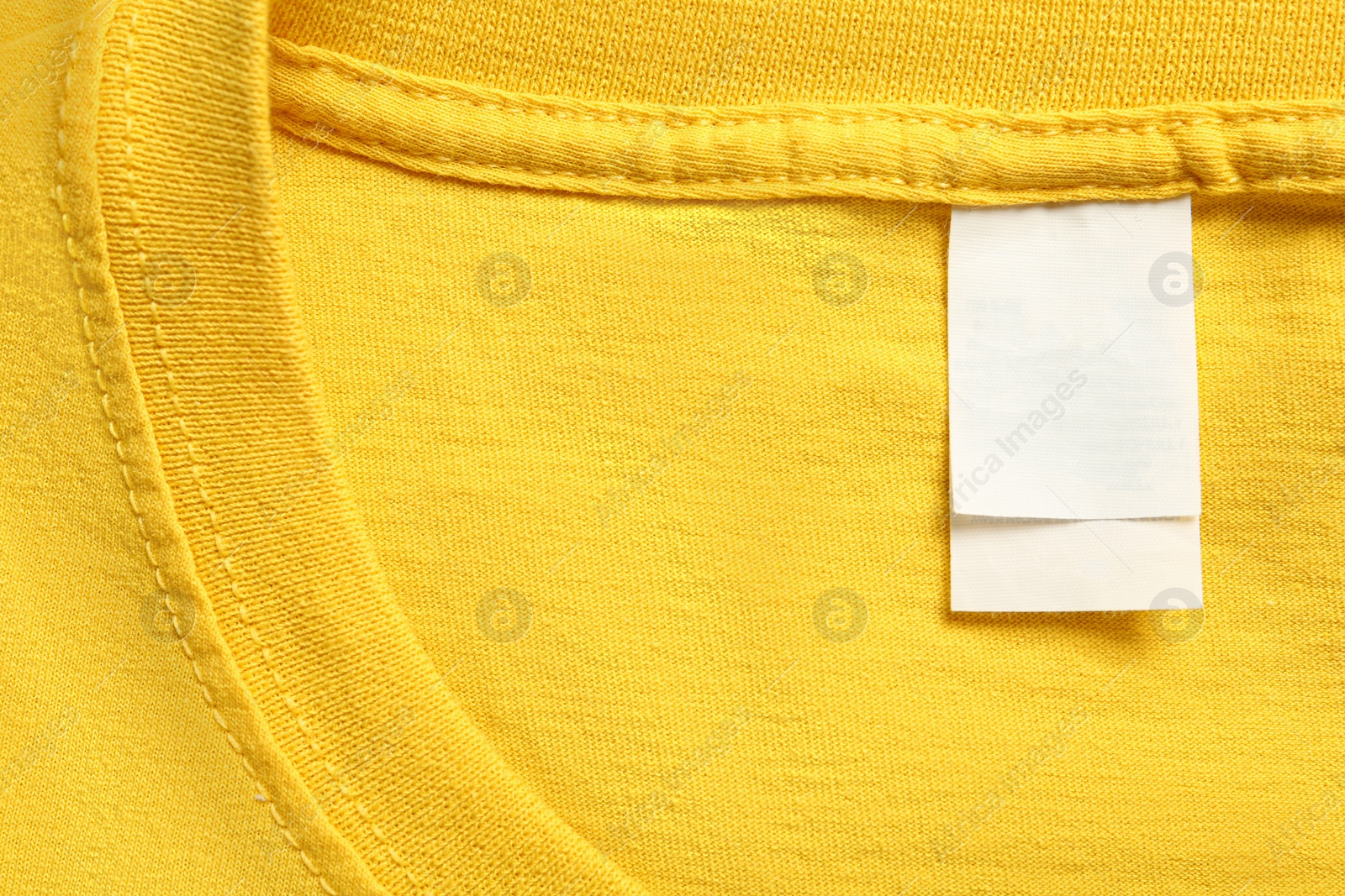 Photo of Blank clothing label on yellow T-shirt, top view