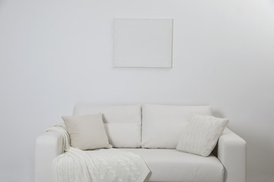 Photo of Blank canvas on wall over comfortable sofa indoors. Space for design