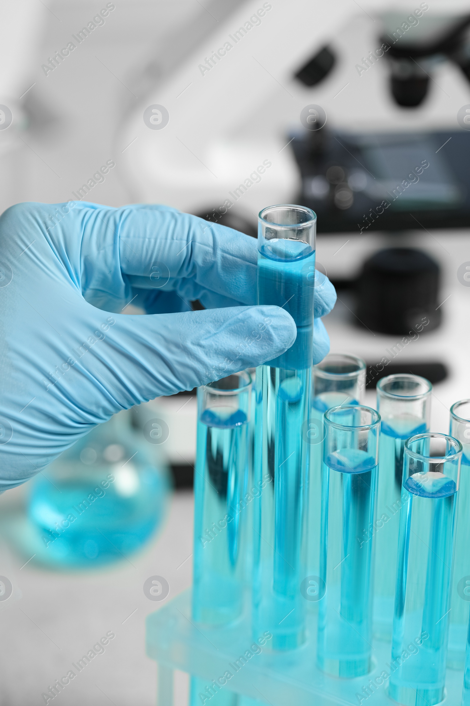 Photo of Scientist taking test tube with light blue liquid in laboratory, closeup