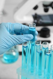 Scientist taking test tube with light blue liquid in laboratory, closeup