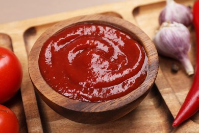 Delicious ketchup in bowl on wooden plate, closeup. Tomato sauce