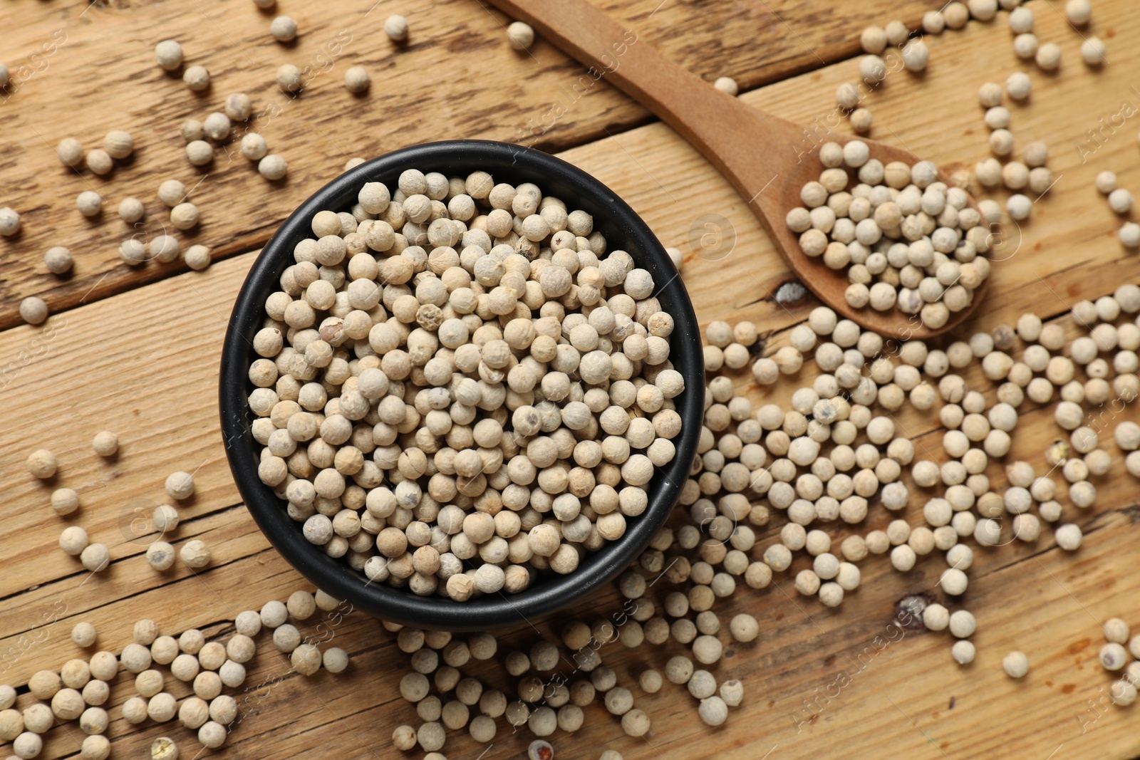 Photo of Aromatic spice. White pepper in bowl and spoon on wooden table, top view