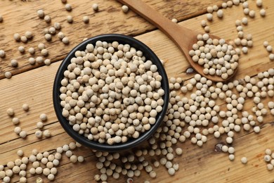 Aromatic spice. White pepper in bowl and spoon on wooden table, top view