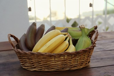 Wicker basket with different sorts of bananas on wooden table