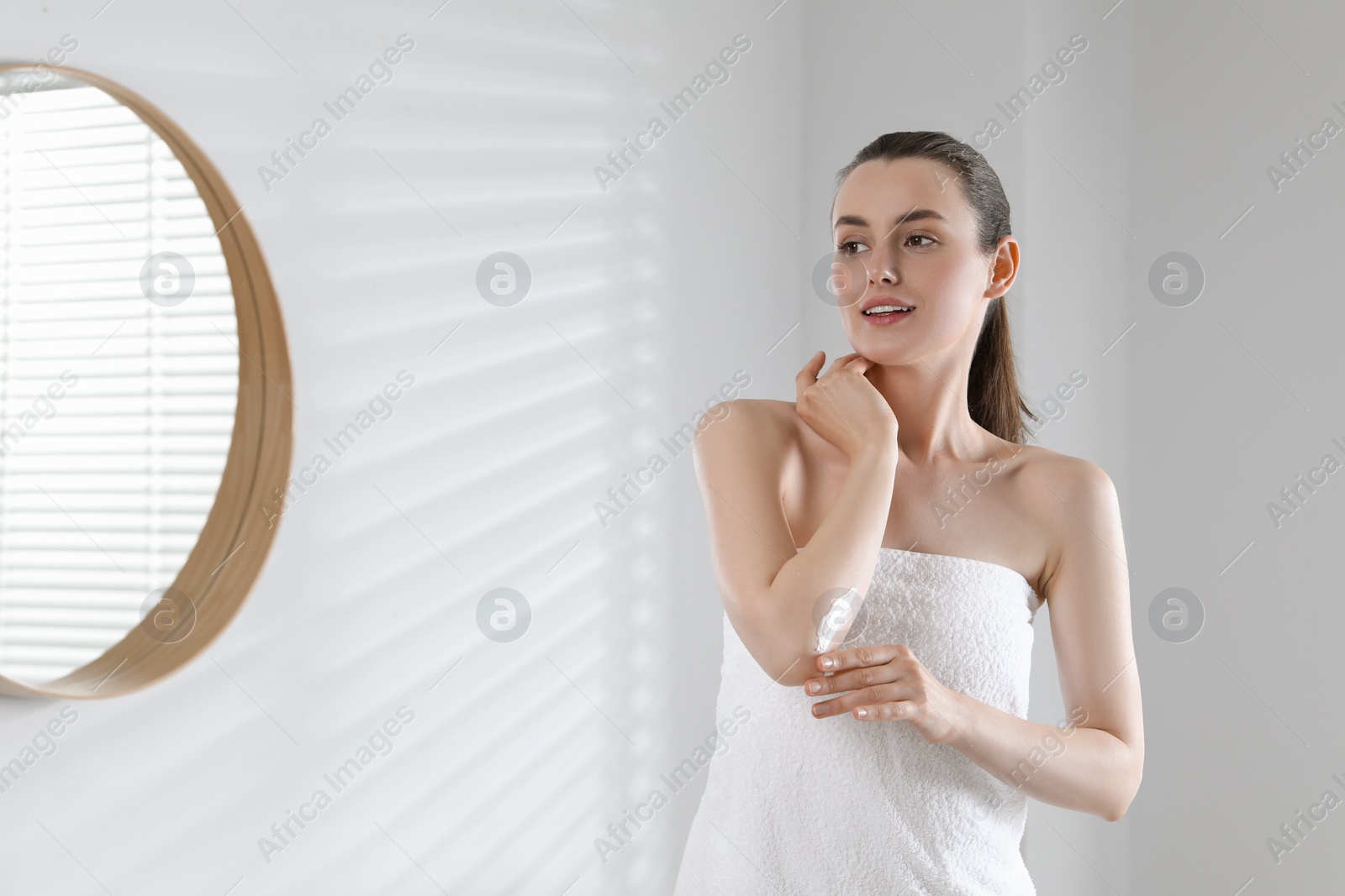Photo of Beautiful woman applying body cream onto elbow in bathroom, space for text