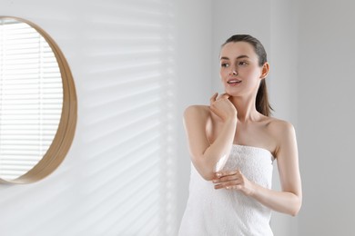 Beautiful woman applying body cream onto elbow in bathroom, space for text