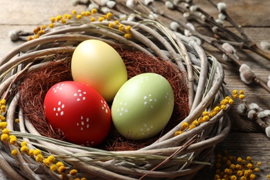 Photo of Colorful painted Easter eggs in wicker nest on table, closeup
