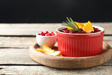 Photo of Cranberry sauce in bowl, fresh berries, rosemary and orange peels on wooden table, space for text