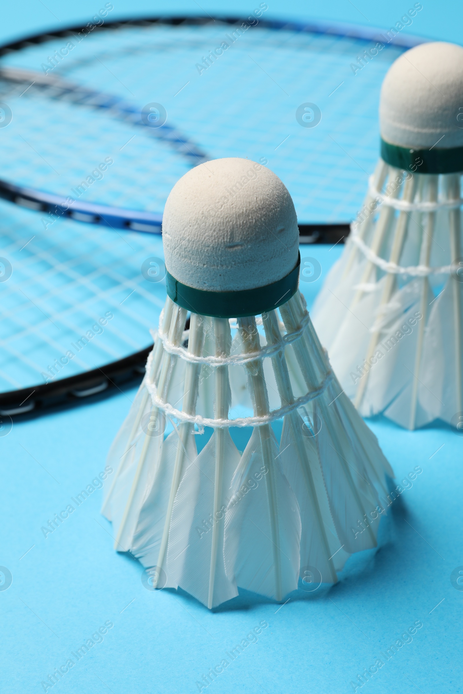 Photo of Feather badminton shuttlecocks and rackets on light blue background, closeup