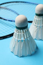 Feather badminton shuttlecocks and rackets on light blue background, closeup