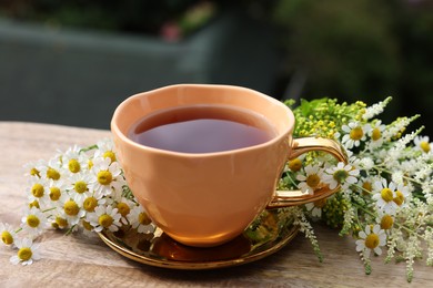 Photo of Cup of delicious chamomile tea and fresh flowers outdoors, closeup