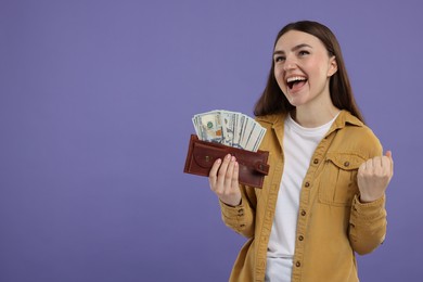 Excited woman holding wallet with dollar banknotes on purple background, space for text